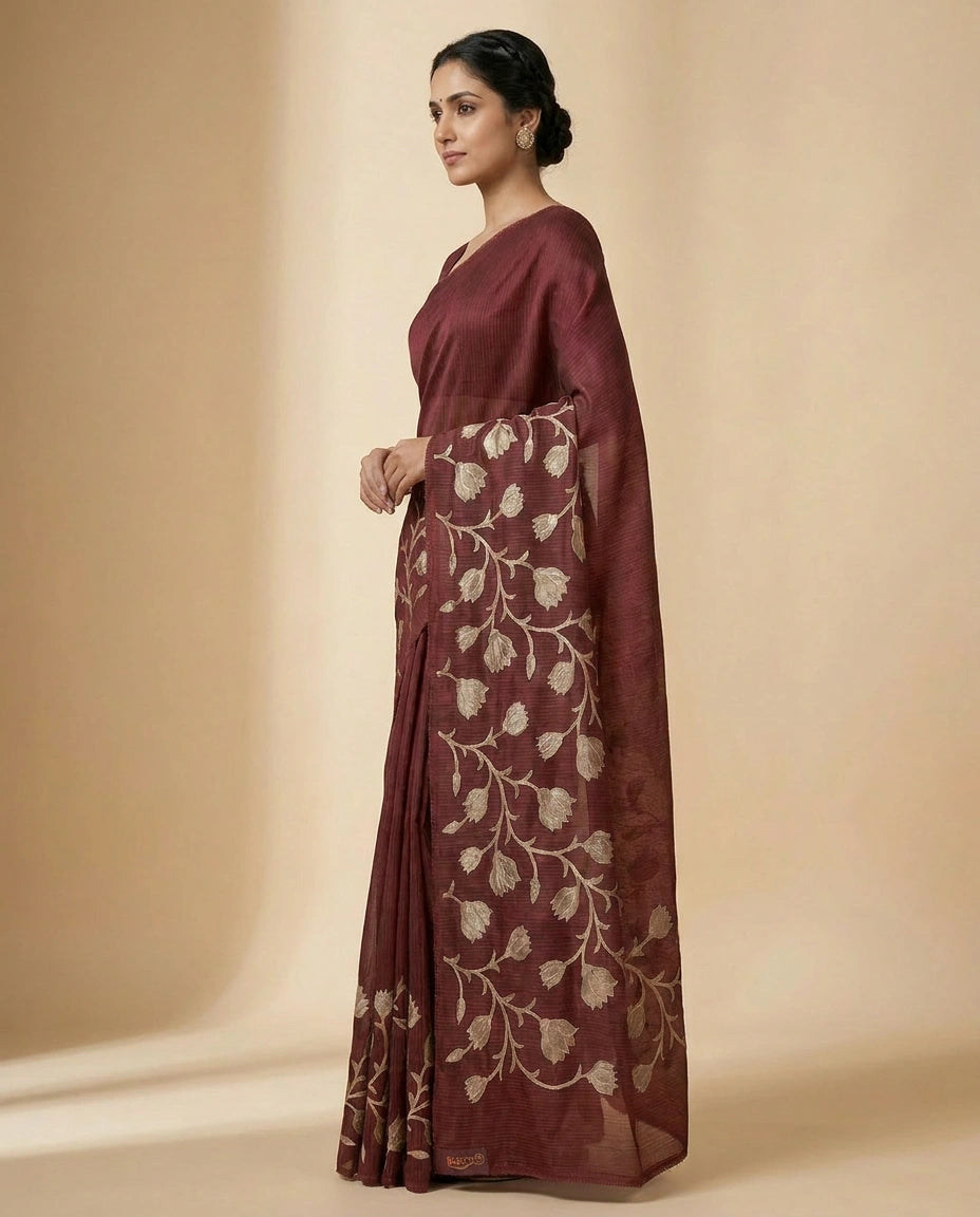 Woman wearing a maroon saree with floral patterns on a beige background