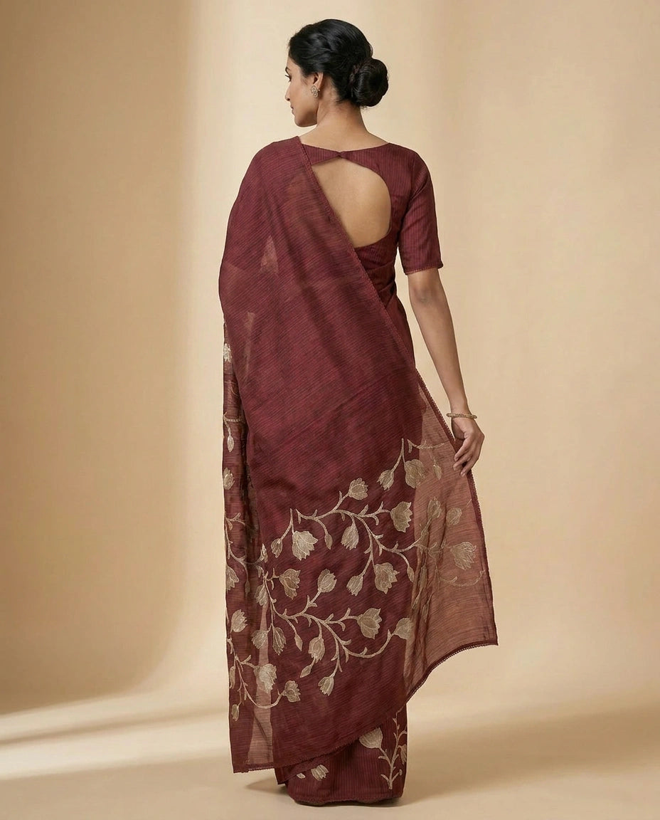 Woman wearing a maroon saree with floral patterns on a beige background