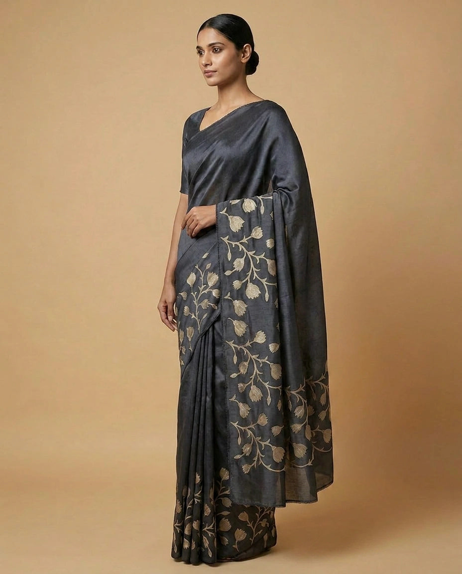 Woman wearing a dark gray saree with floral patterns on a beige background