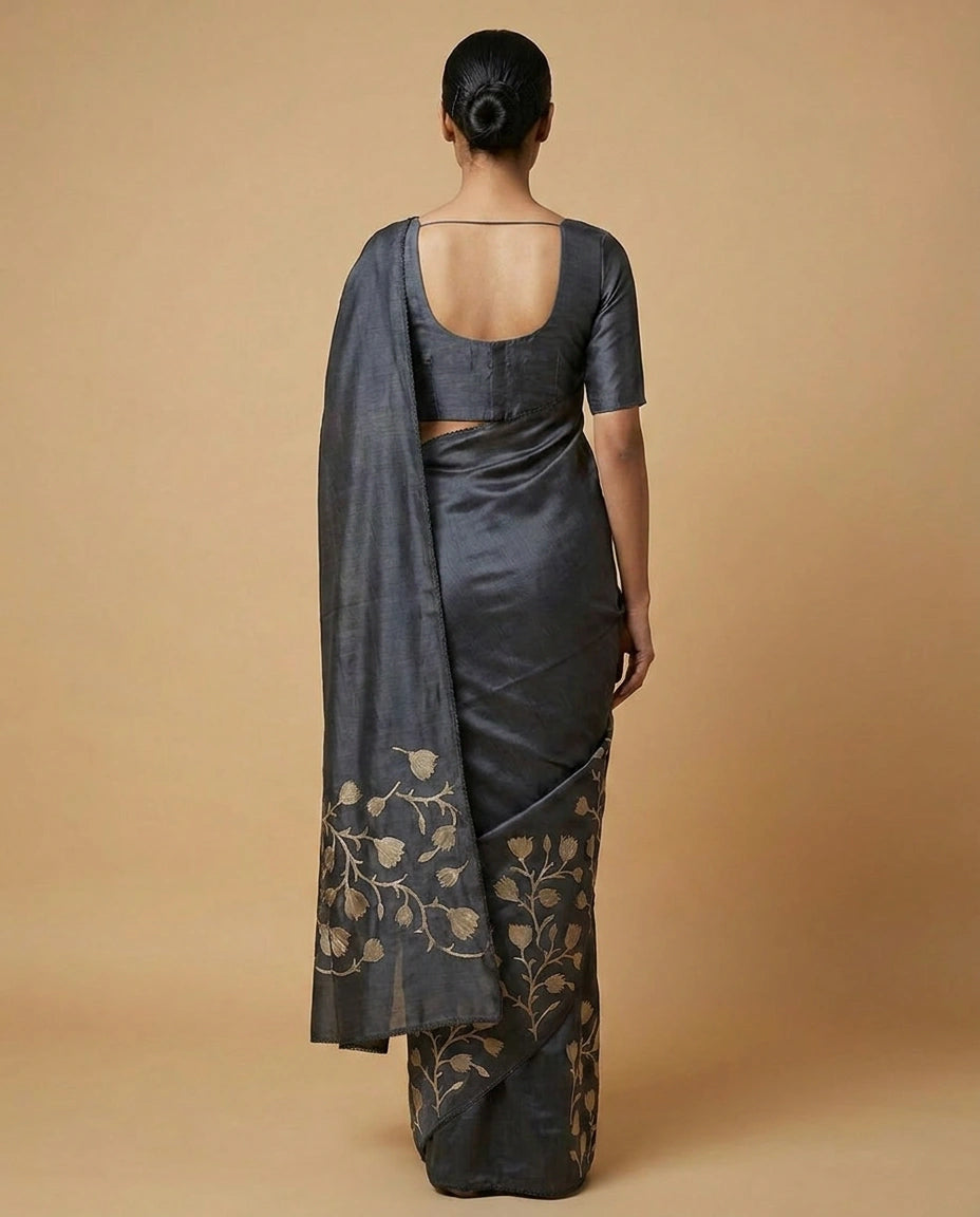 Woman wearing a dark gray saree with floral patterns on a beige background
