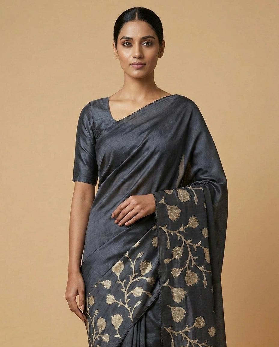 Woman wearing a dark gray saree with floral patterns on a beige background