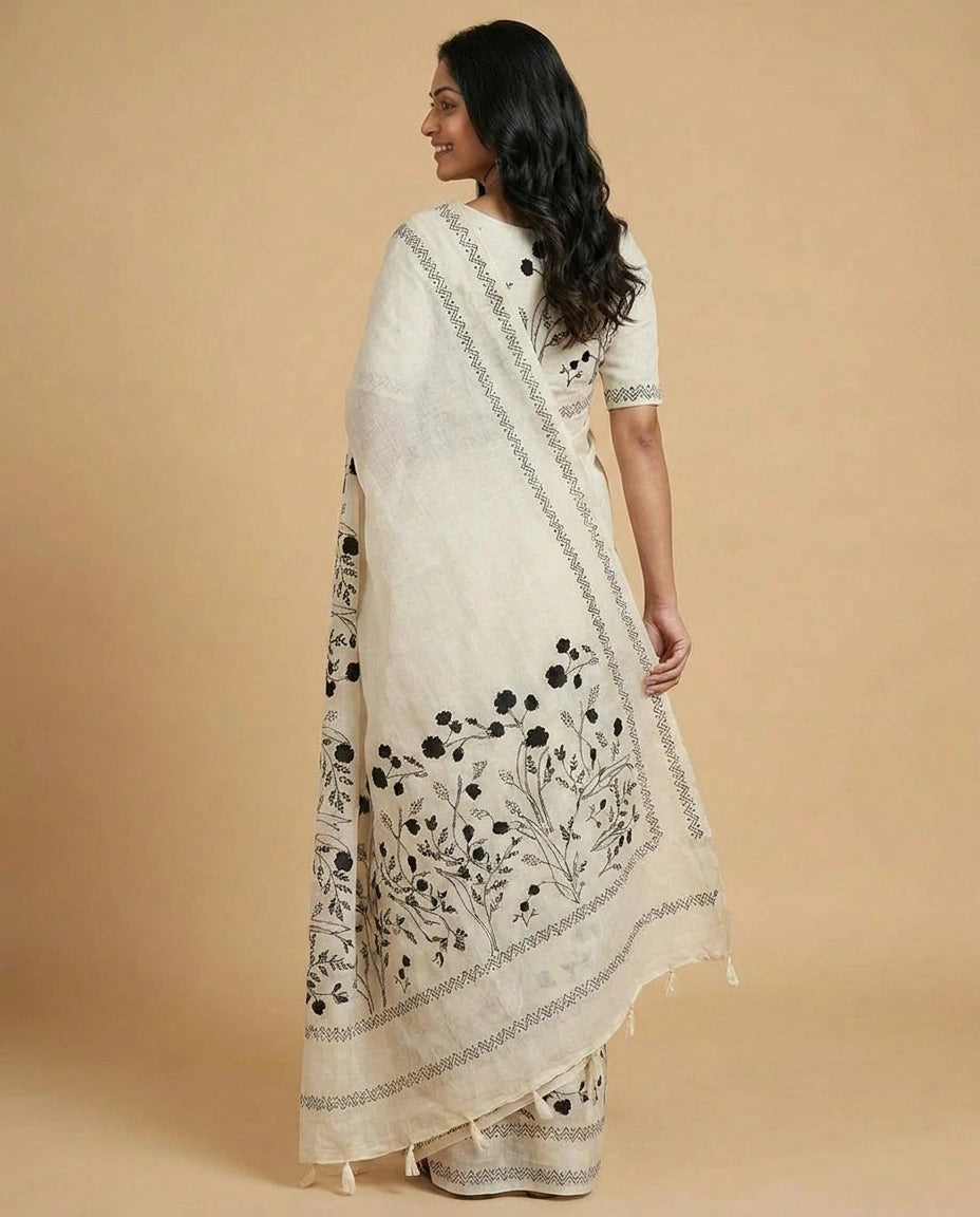 Woman wearing a white saree with black floral embroidery on a beige background