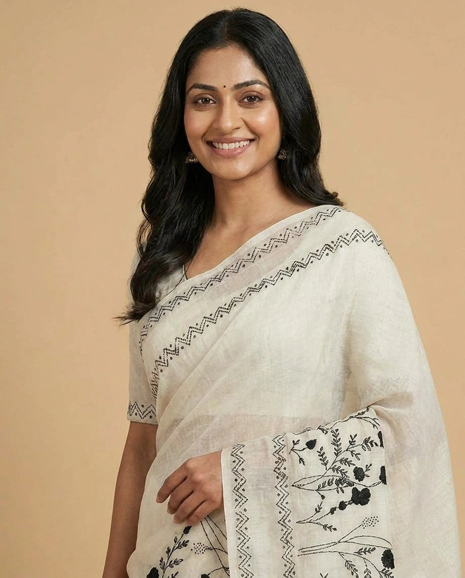 Woman wearing a white saree with black patterns on a beige background