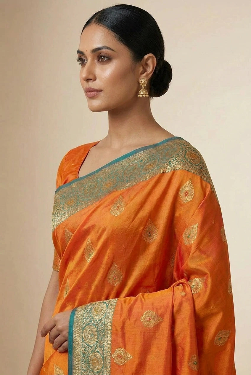 Woman wearing an orange saree with a gold border on a beige background