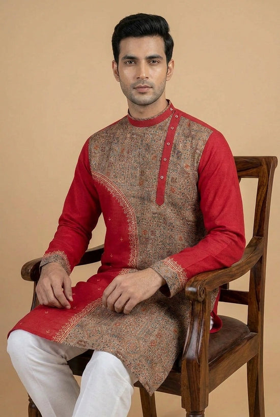 Man wearing a red and brown traditional kurta sitting on a wooden chair against a beige background