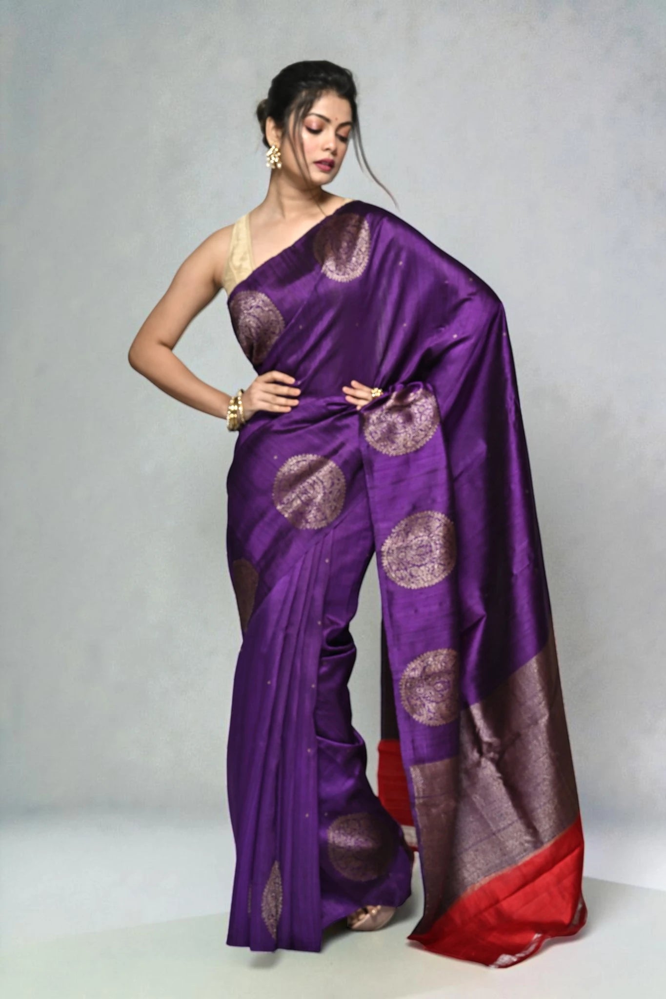 Woman wearing a purple saree with gold patterns on a plain background