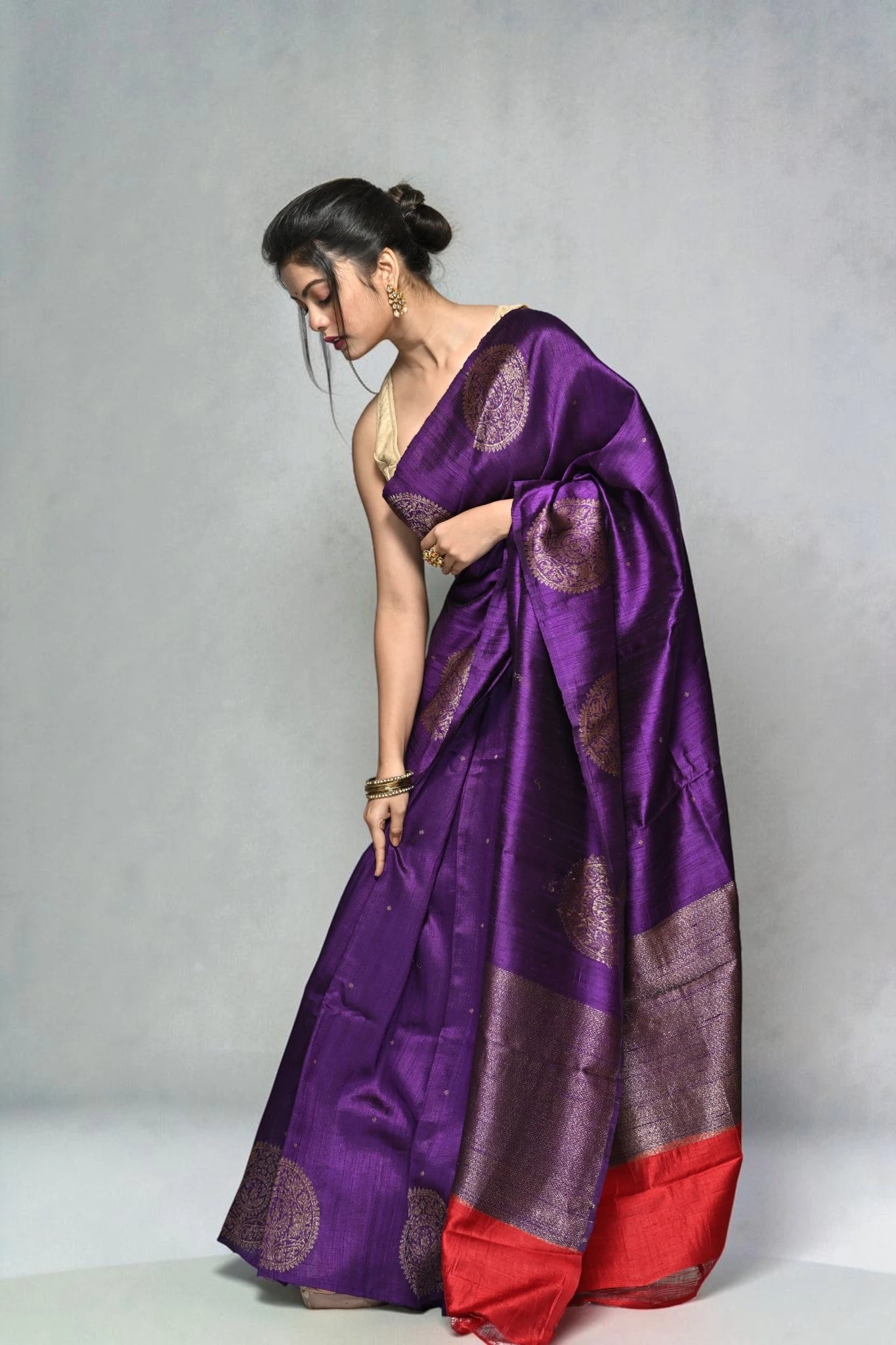 Woman wearing a purple saree with a red border against a gray background