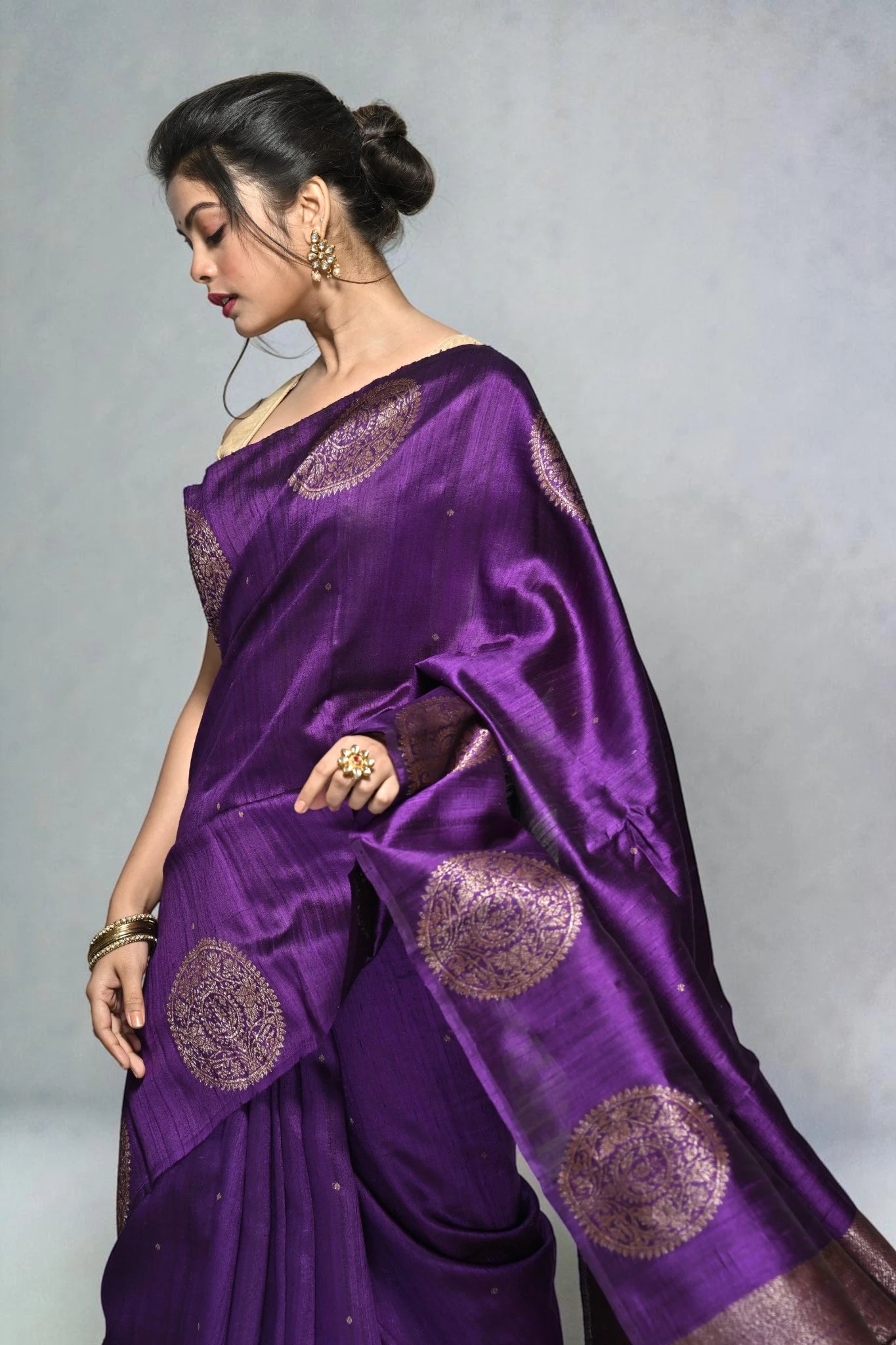 Woman wearing a purple saree with gold patterns on a gray background