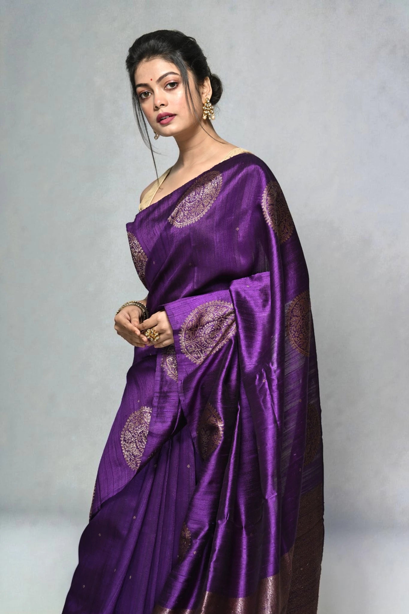 Woman wearing a purple saree with intricate designs on a gray background