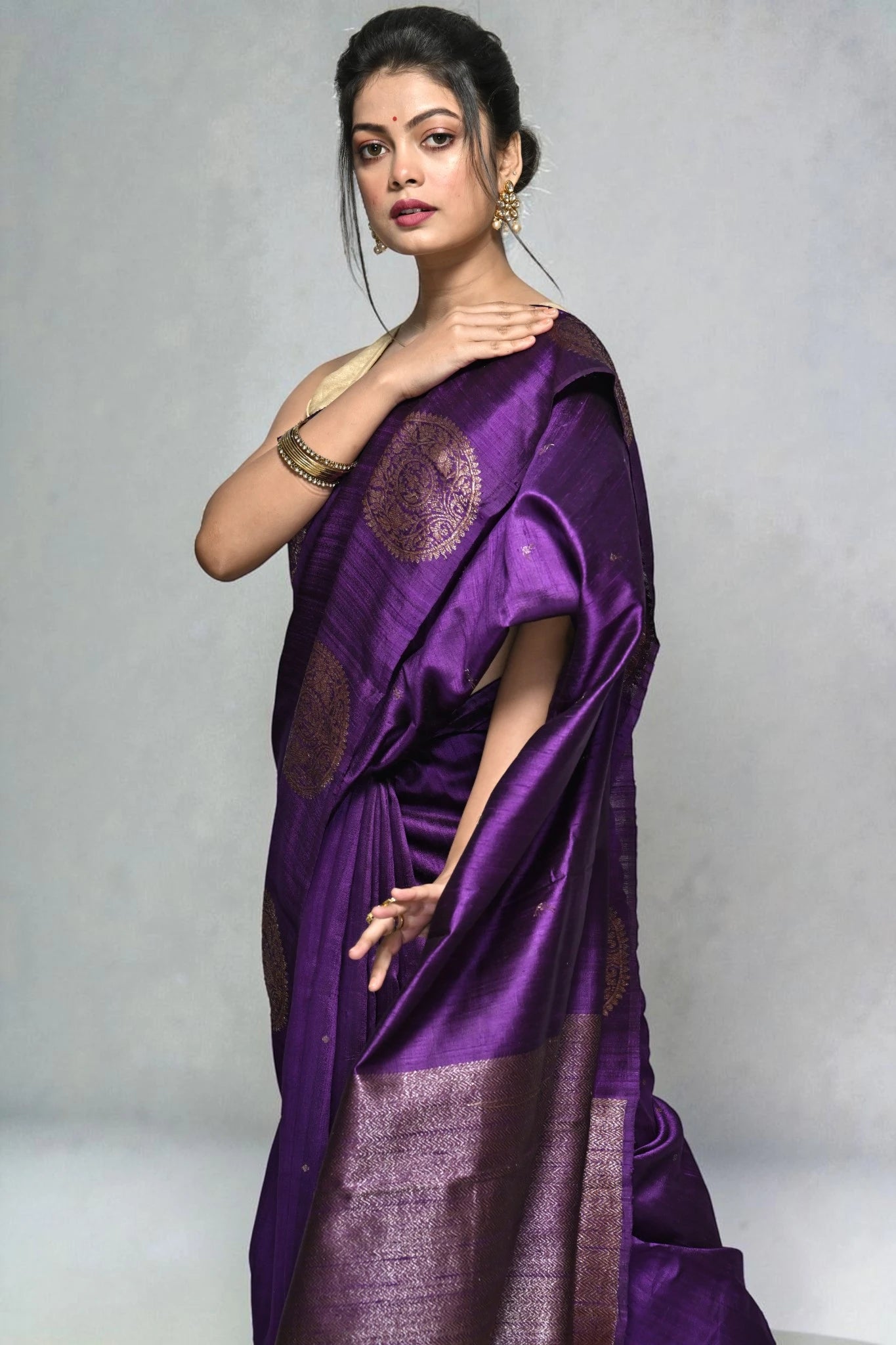Woman wearing a purple saree with a decorative pattern on a plain background