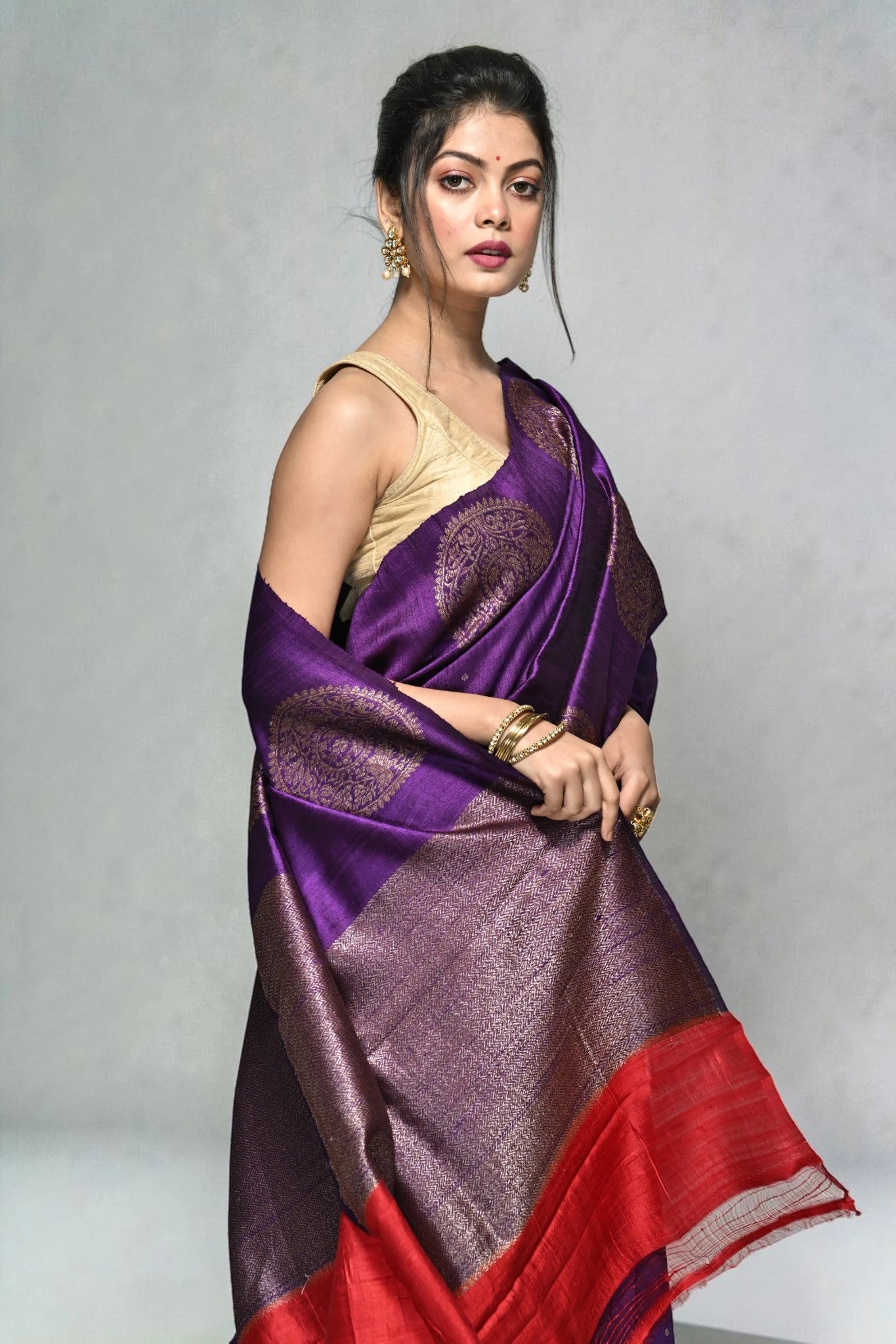 Woman wearing a purple and red saree with a plain background
