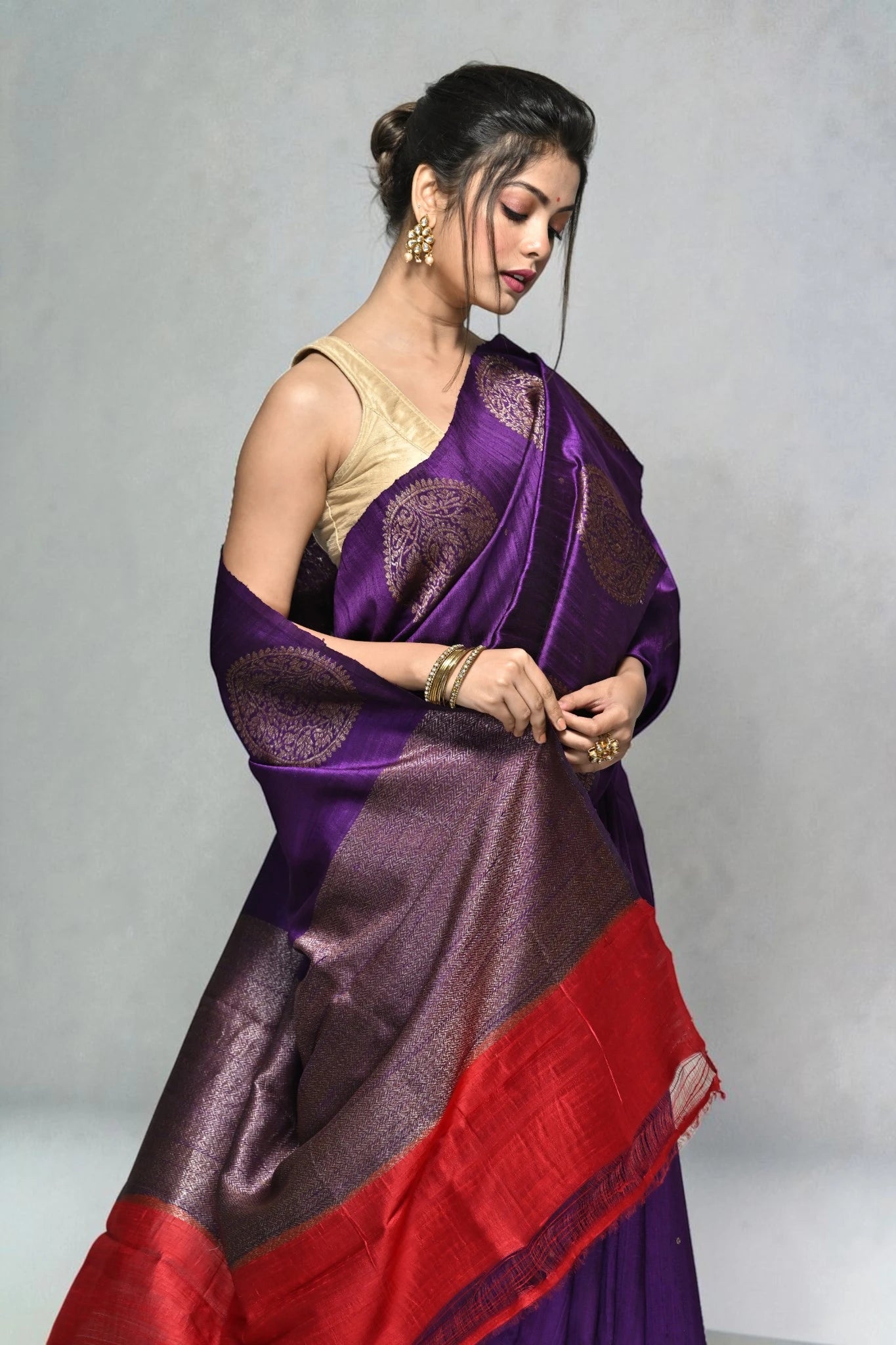 Woman wearing a purple and red saree with a plain background