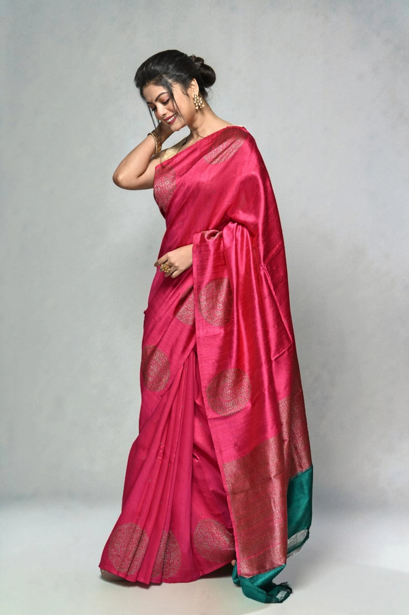 Woman wearing a pink saree with a green border on a plain background