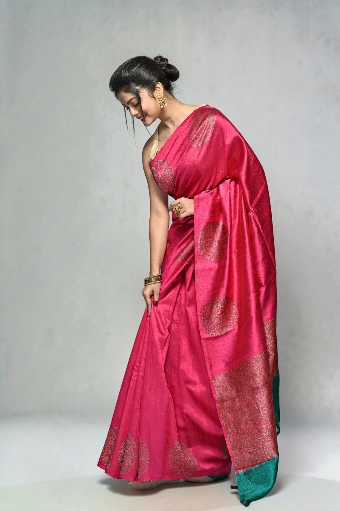 Woman wearing a pink saree with a green border on a plain background