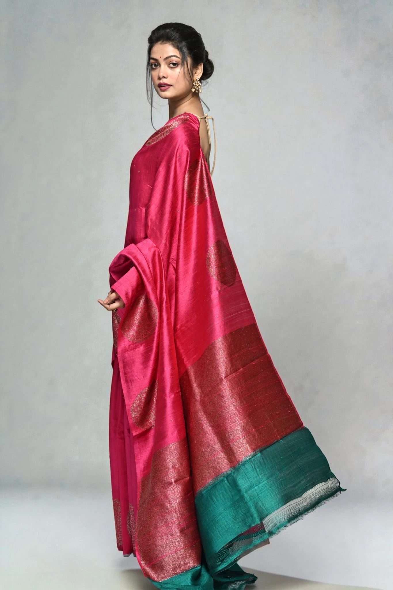 Woman wearing a pink saree with a green border on a plain background