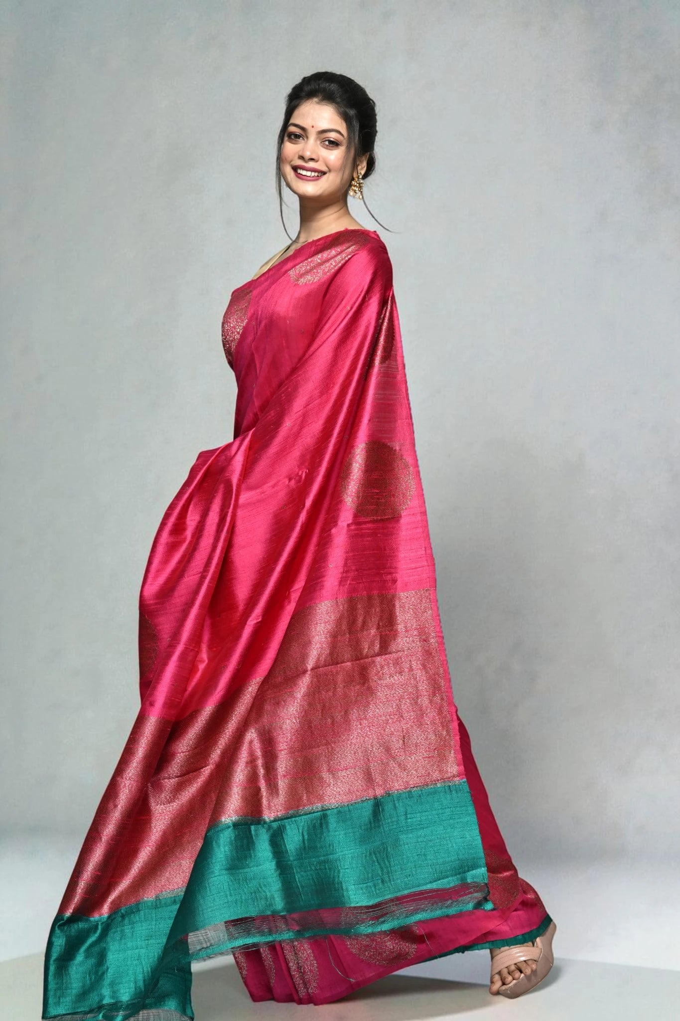 Woman wearing a pink saree with green border on a plain background