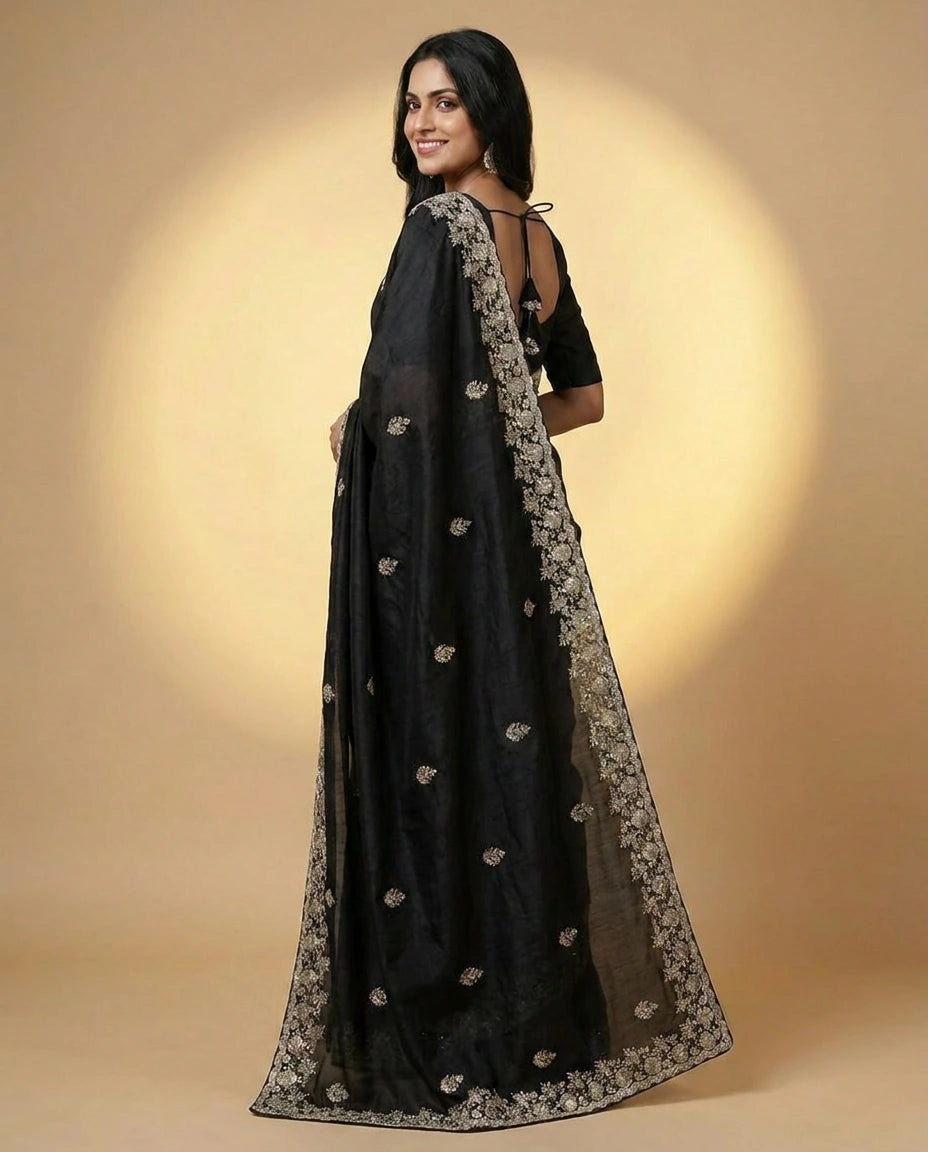 Woman wearing a black saree with a floral pattern on a beige background