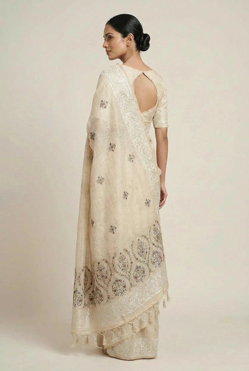 Woman wearing a cream-colored embroidered saree with a plain background