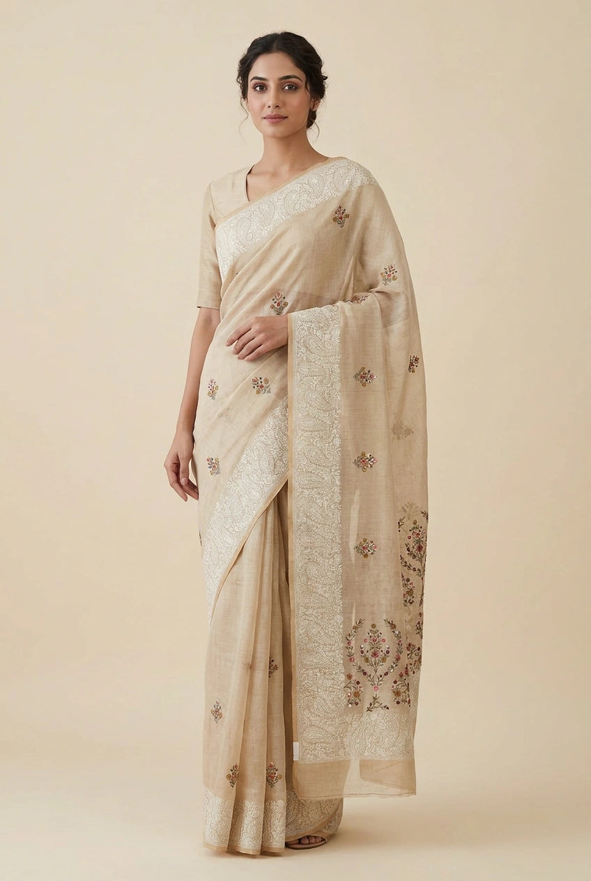 Woman wearing a beige saree with intricate patterns on a beige background