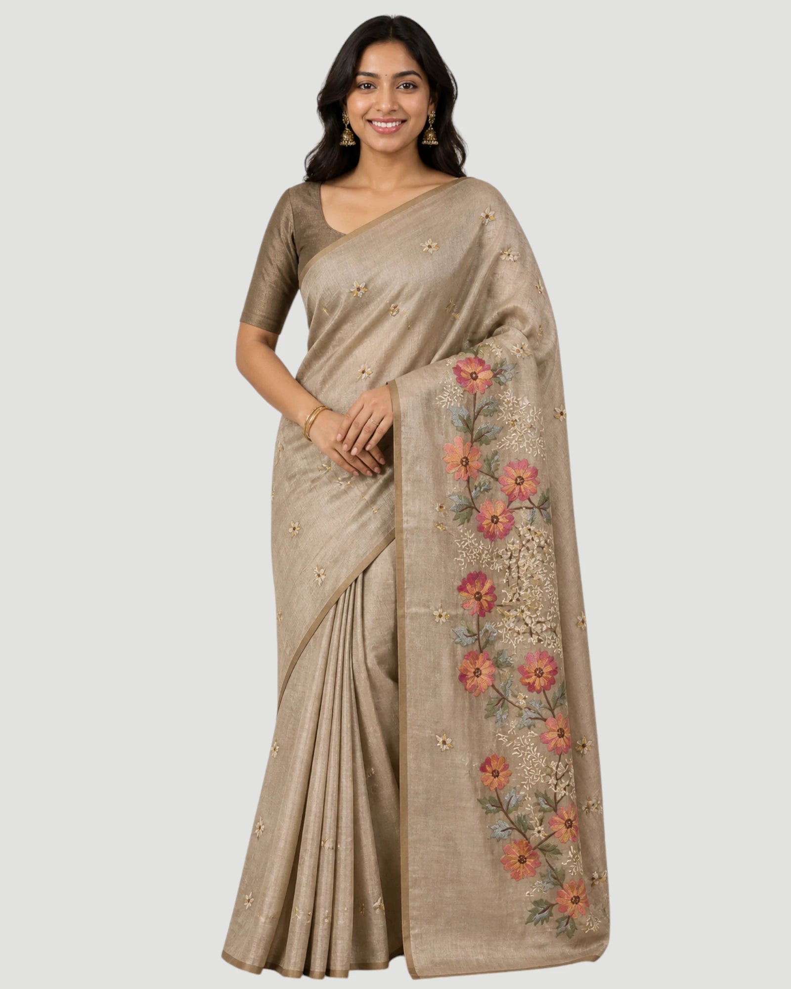 Woman wearing a beige saree with floral embroidery on a plain background
