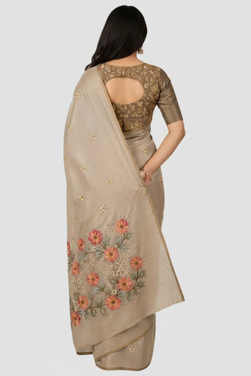 Woman wearing a beige saree with floral embroidery on a plain background
