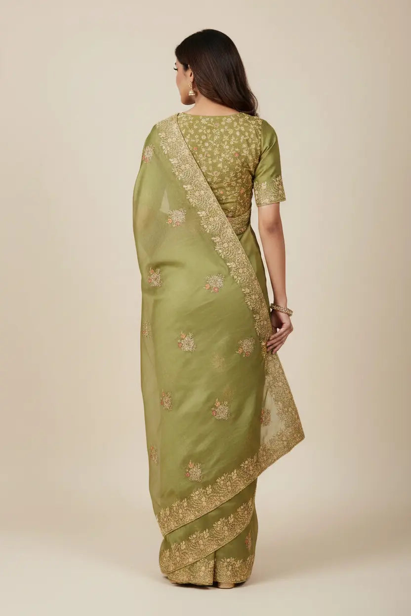 Woman wearing a green saree with gold patterns on a beige background