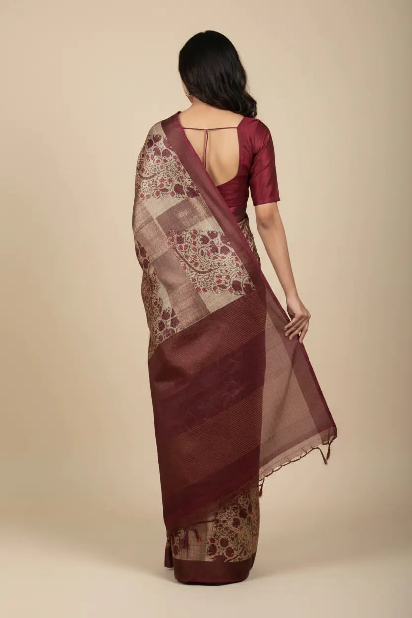 Woman wearing a maroon saree with a patterned blouse on a beige background
