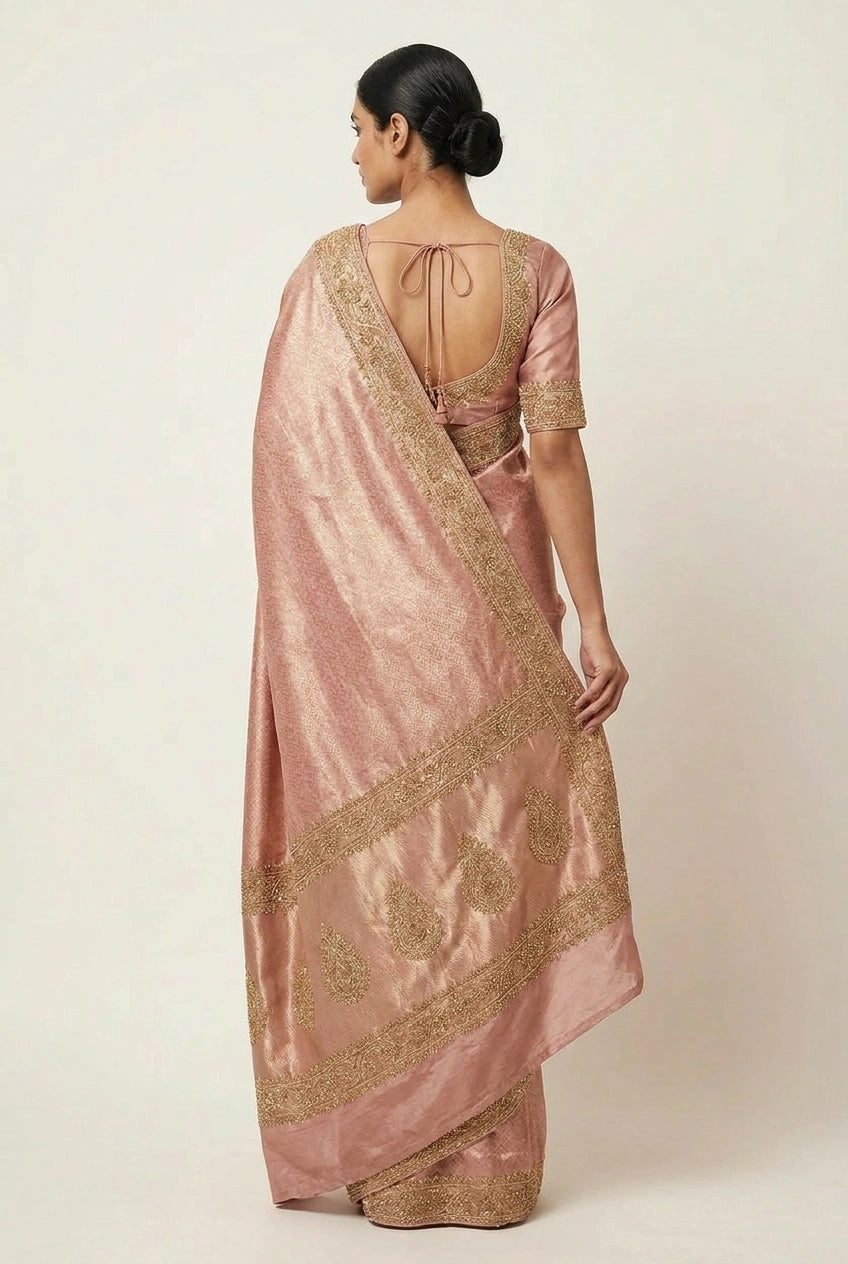 Woman wearing a pink saree with gold embroidery on a plain background