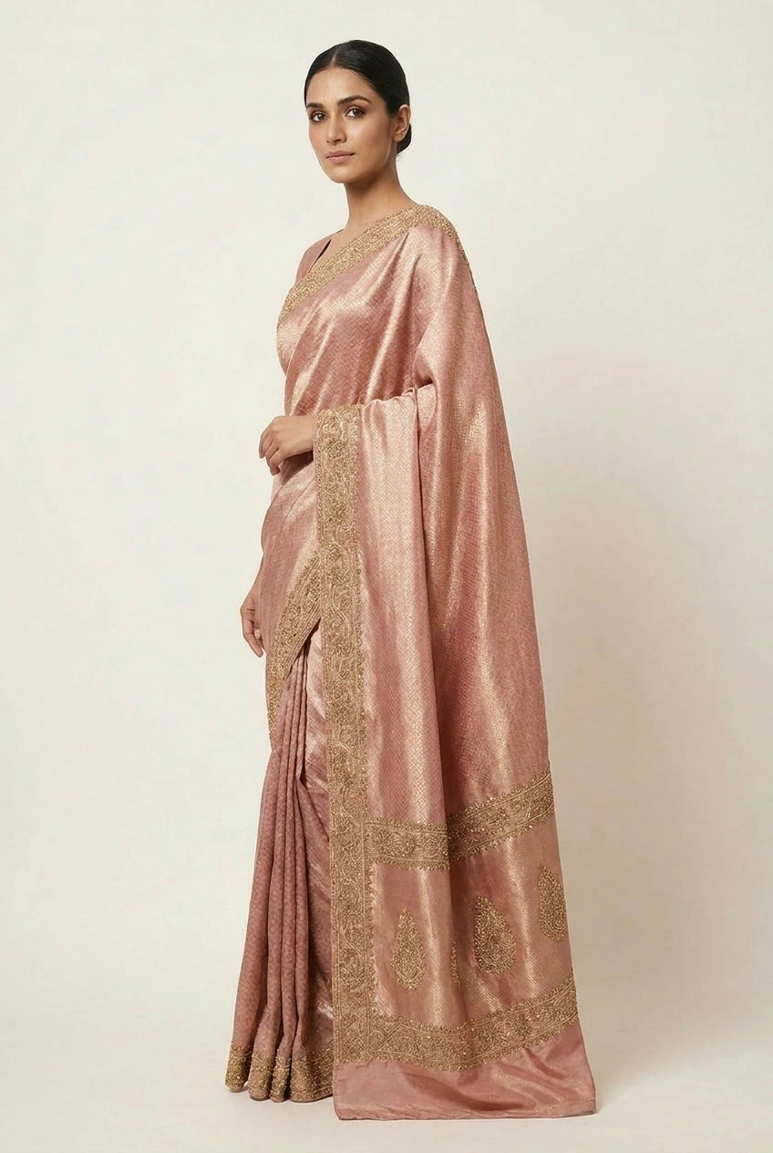 Woman wearing a pink saree with gold embroidery on a white background