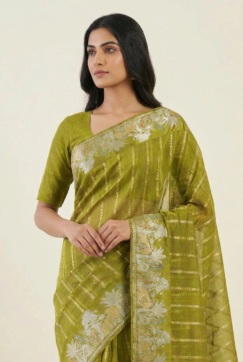Woman wearing a green saree with white patterns on a plain background