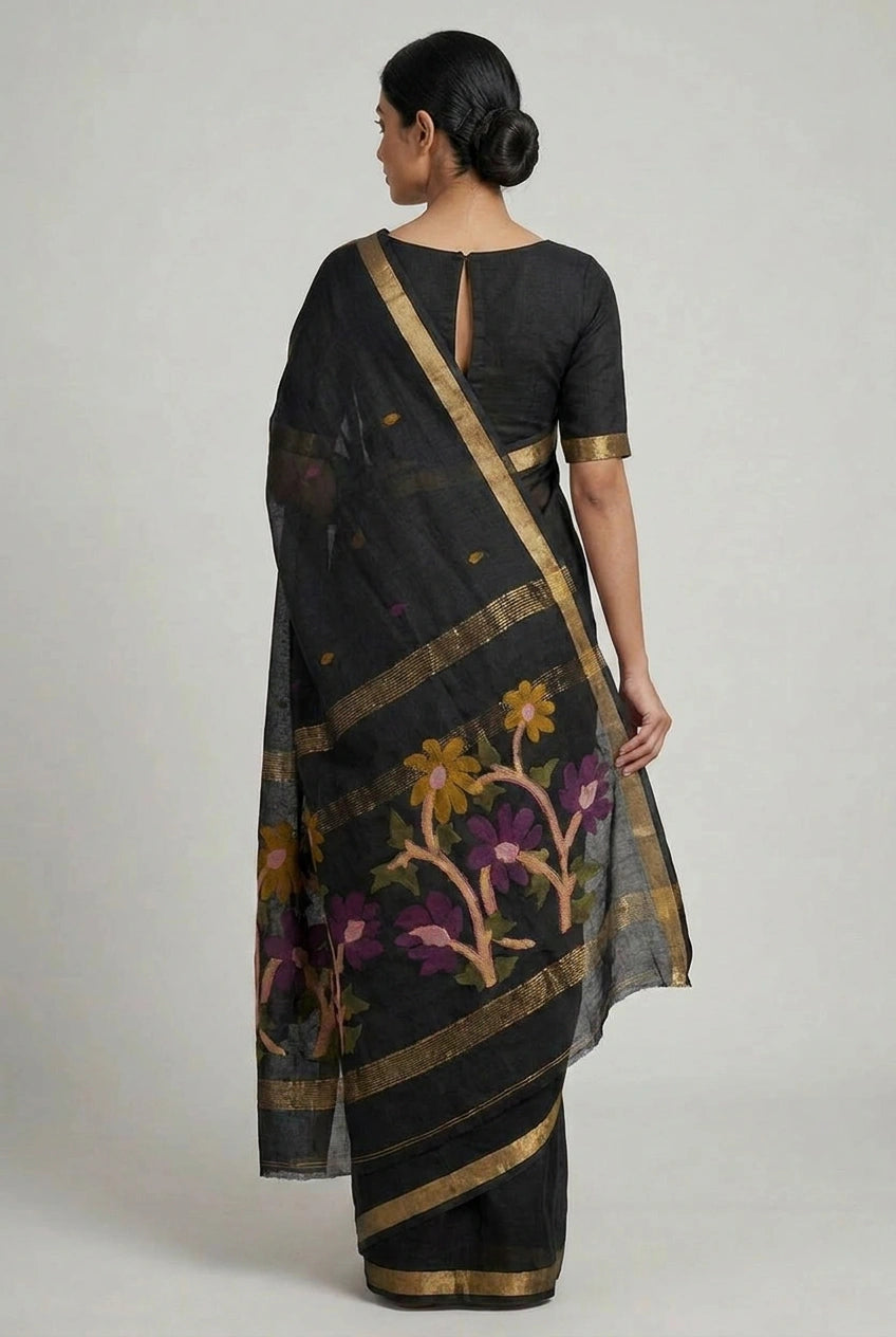 Woman wearing a black saree with floral patterns and gold accents on a plain background