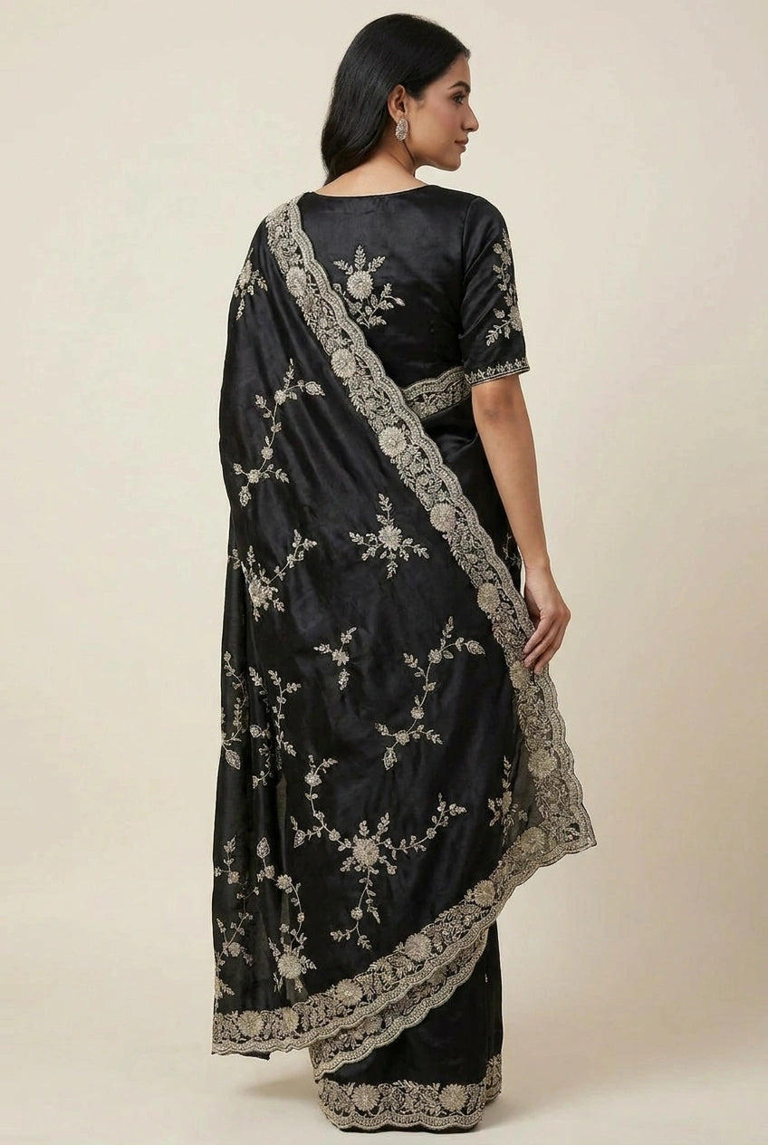 Woman wearing a black saree with silver embroidery on a plain background