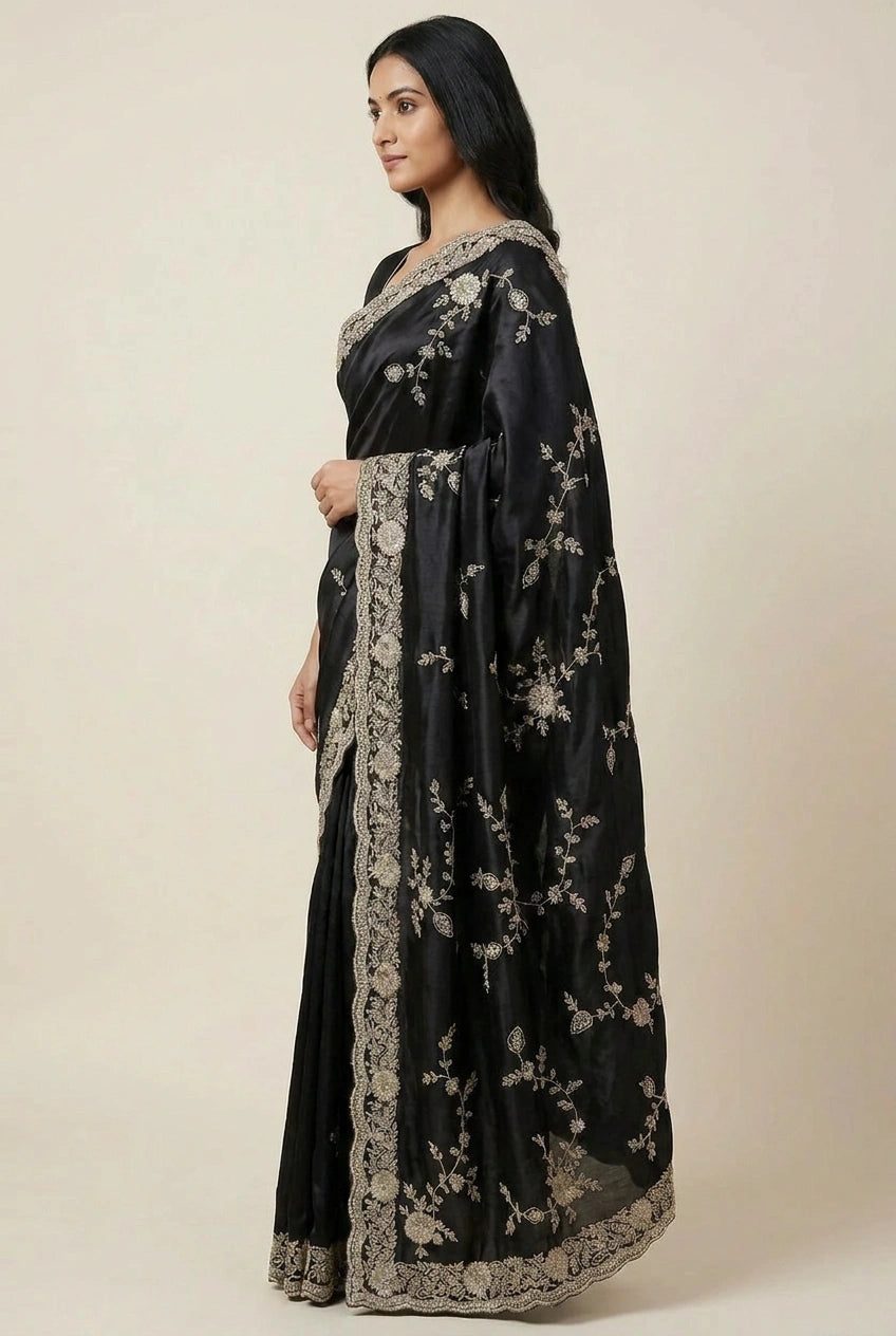 Woman wearing a black saree with floral patterns on a plain background