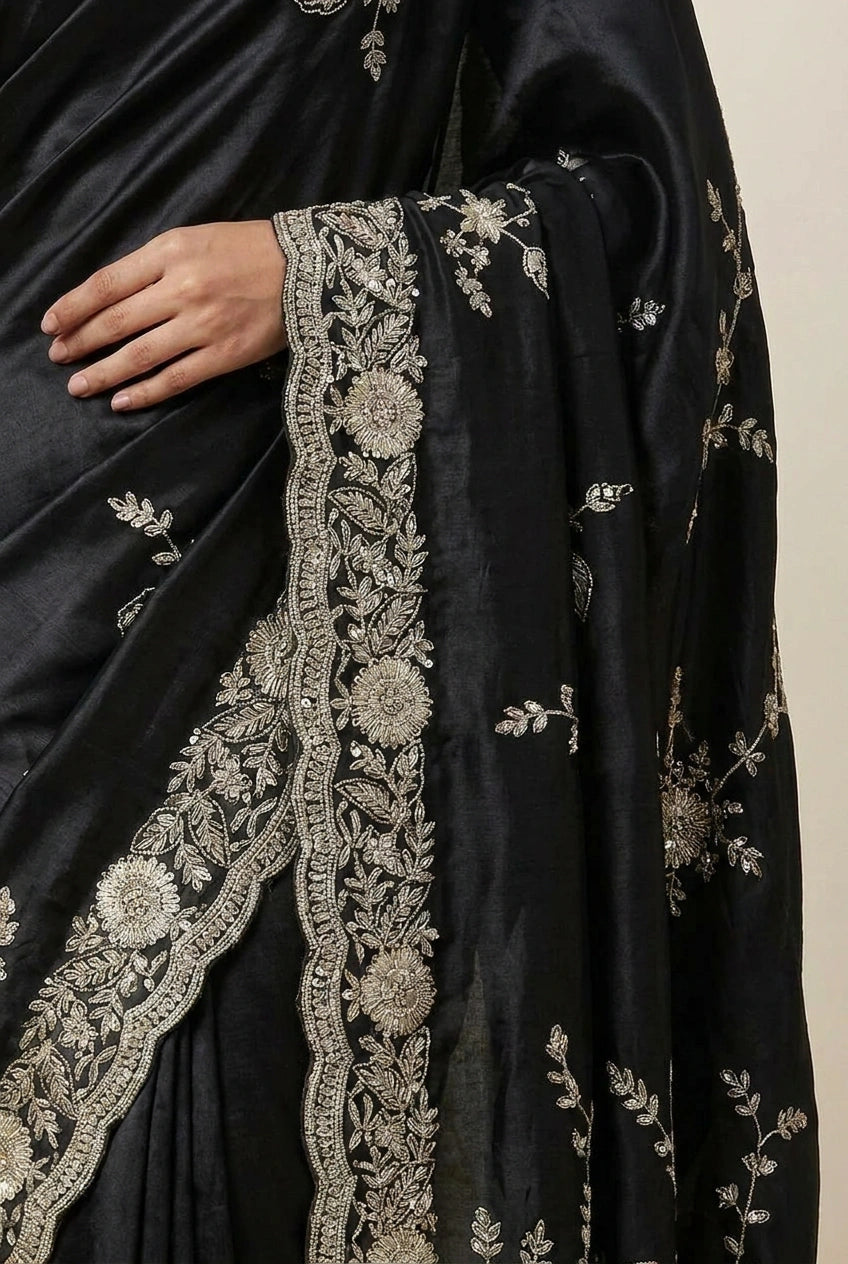 Black saree with intricate silver embroidery on a beige background