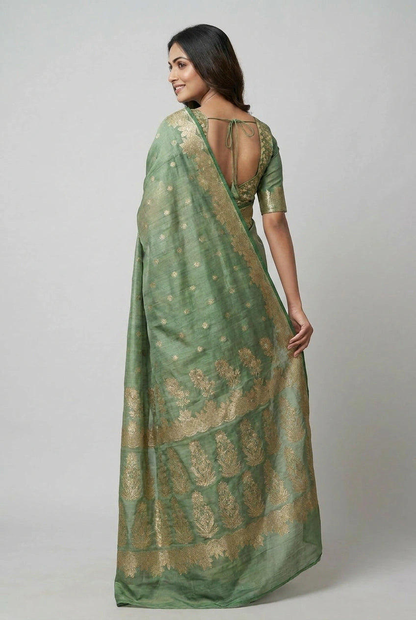 Woman wearing a green saree with gold patterns on a plain background