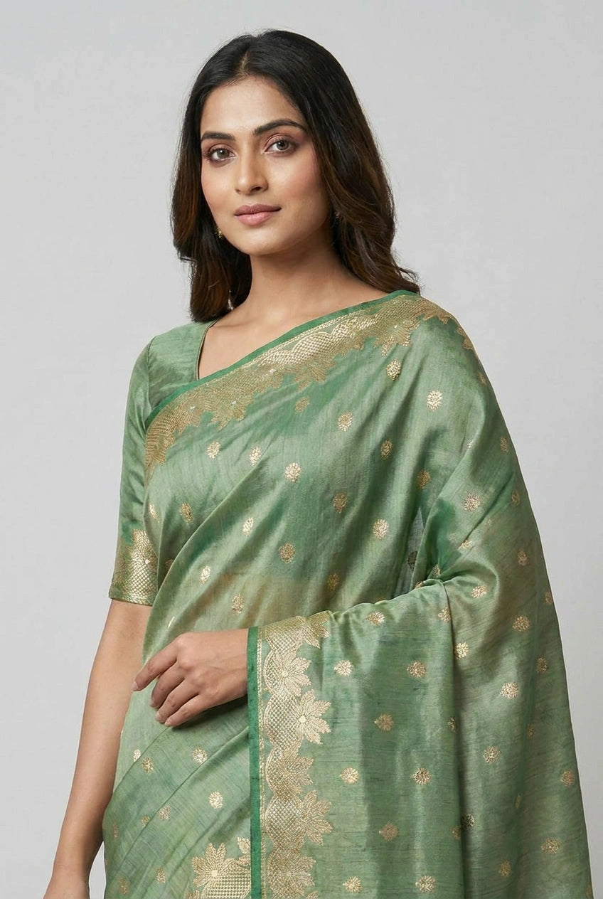 Woman wearing a green saree with gold patterns on a light gray background