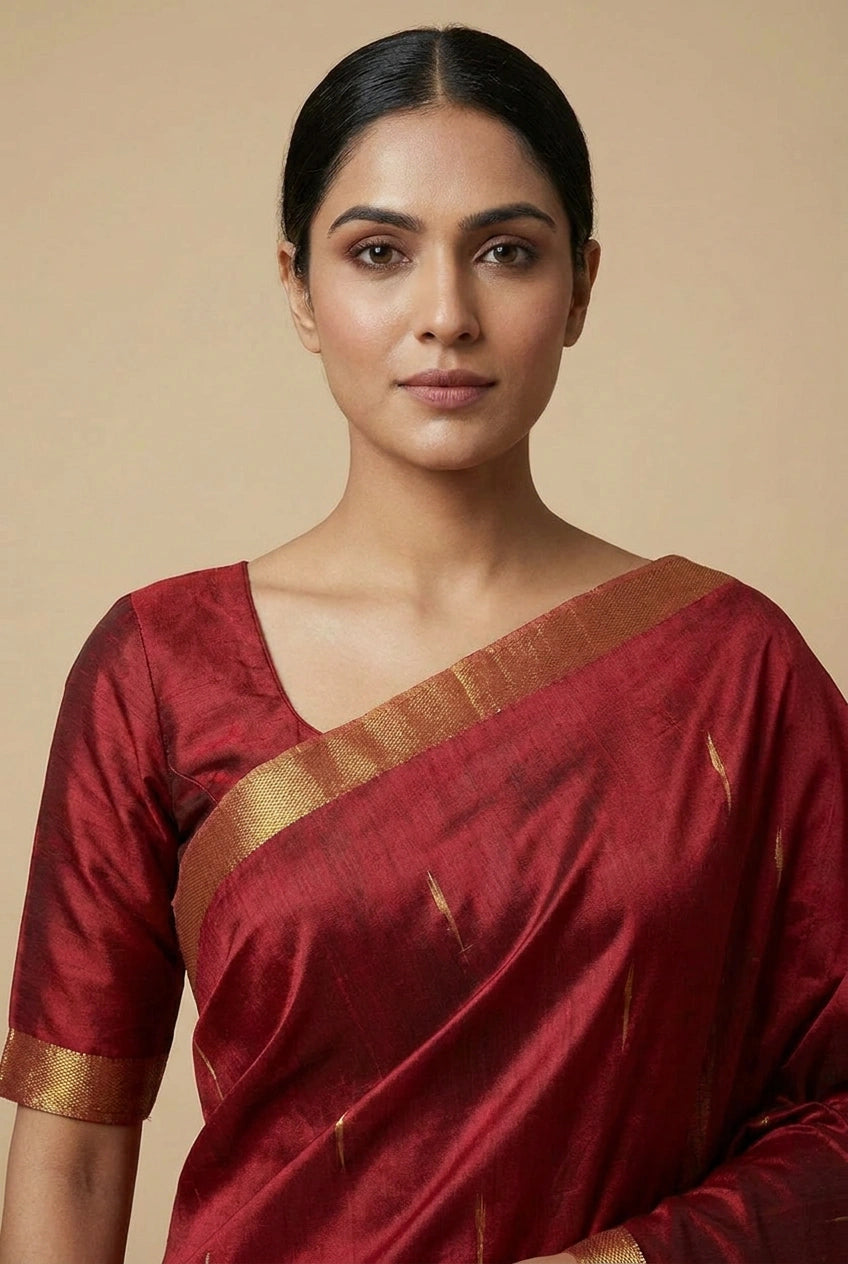 Woman wearing a red saree with gold border against a beige background