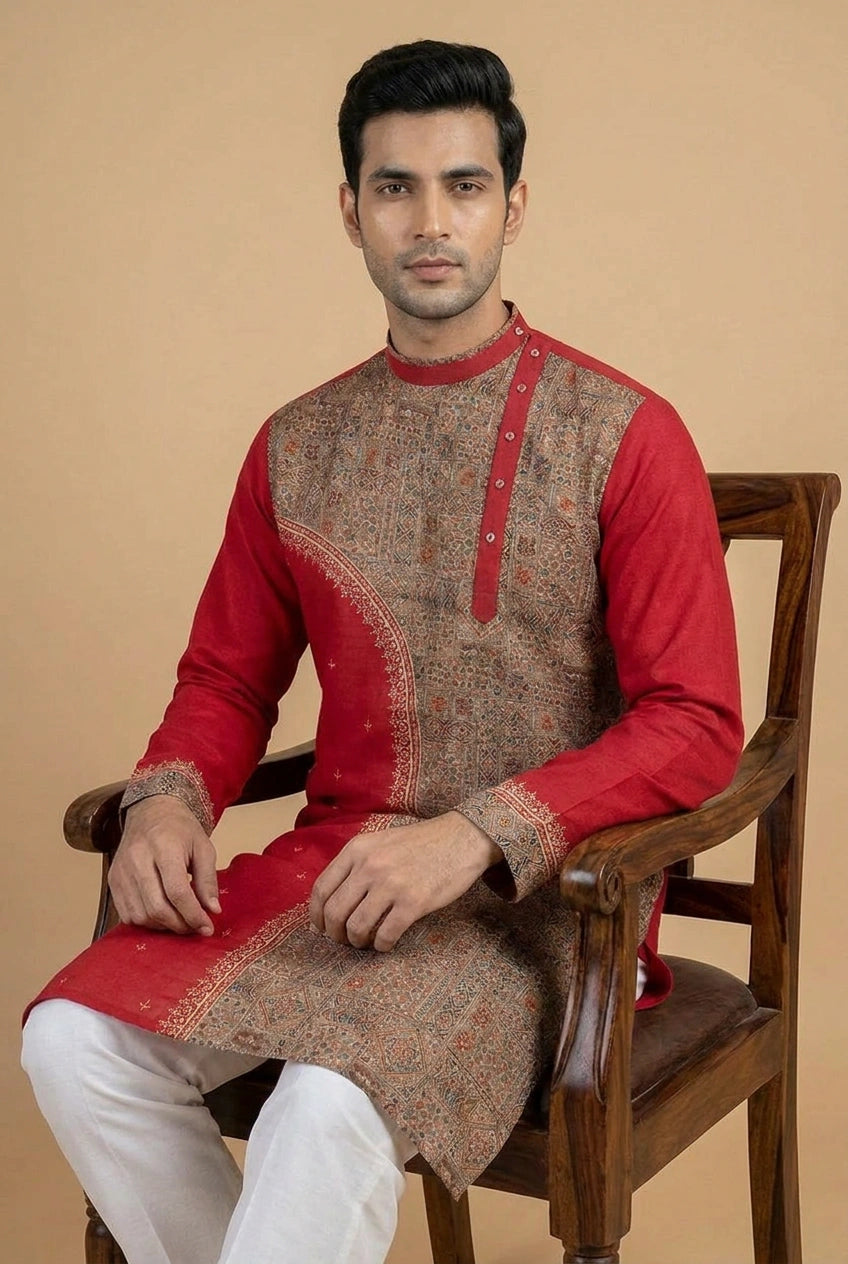 Man wearing a red and brown traditional kurta sitting on a wooden chair against a beige background