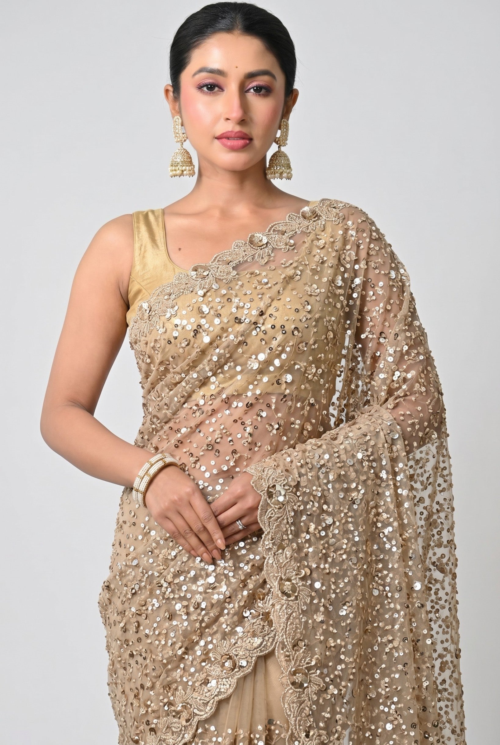 Rangoli champagne net saree with shimmering sequins and intricate floral embroidery on the border. Perfect for festive occasions.