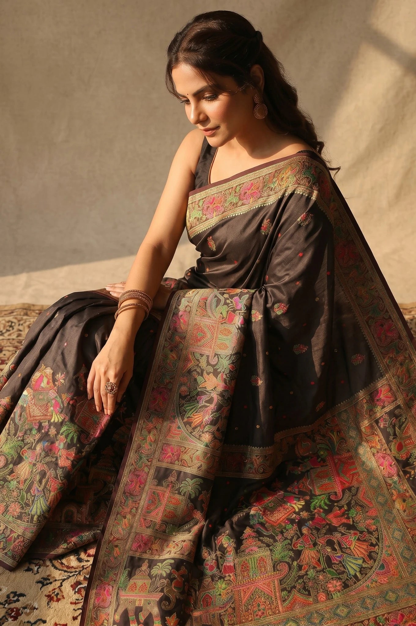 Woman wearing a traditional saree with intricate patterns, sitting on a textured floor.