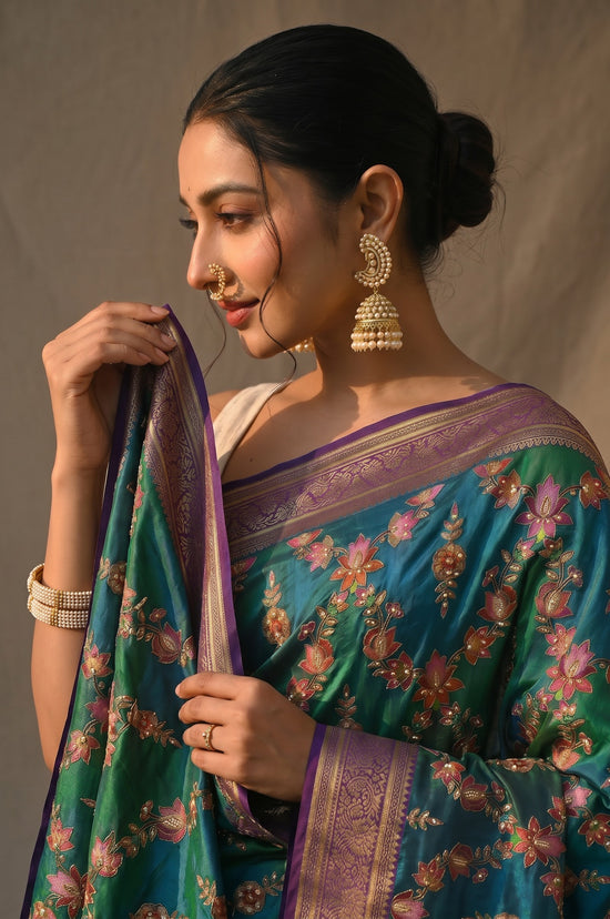 Rangoli teal and emerald green silk saree with floral embroidery, sequins, and purple border with gold motifs.