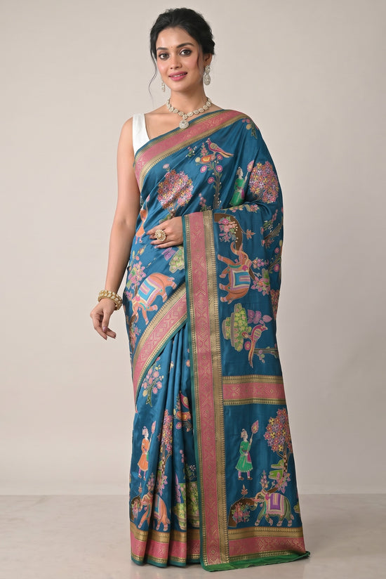 Rangoli teal silk saree with intricate motifs of elephants, birds, and floral designs. Features pink and gold borders.