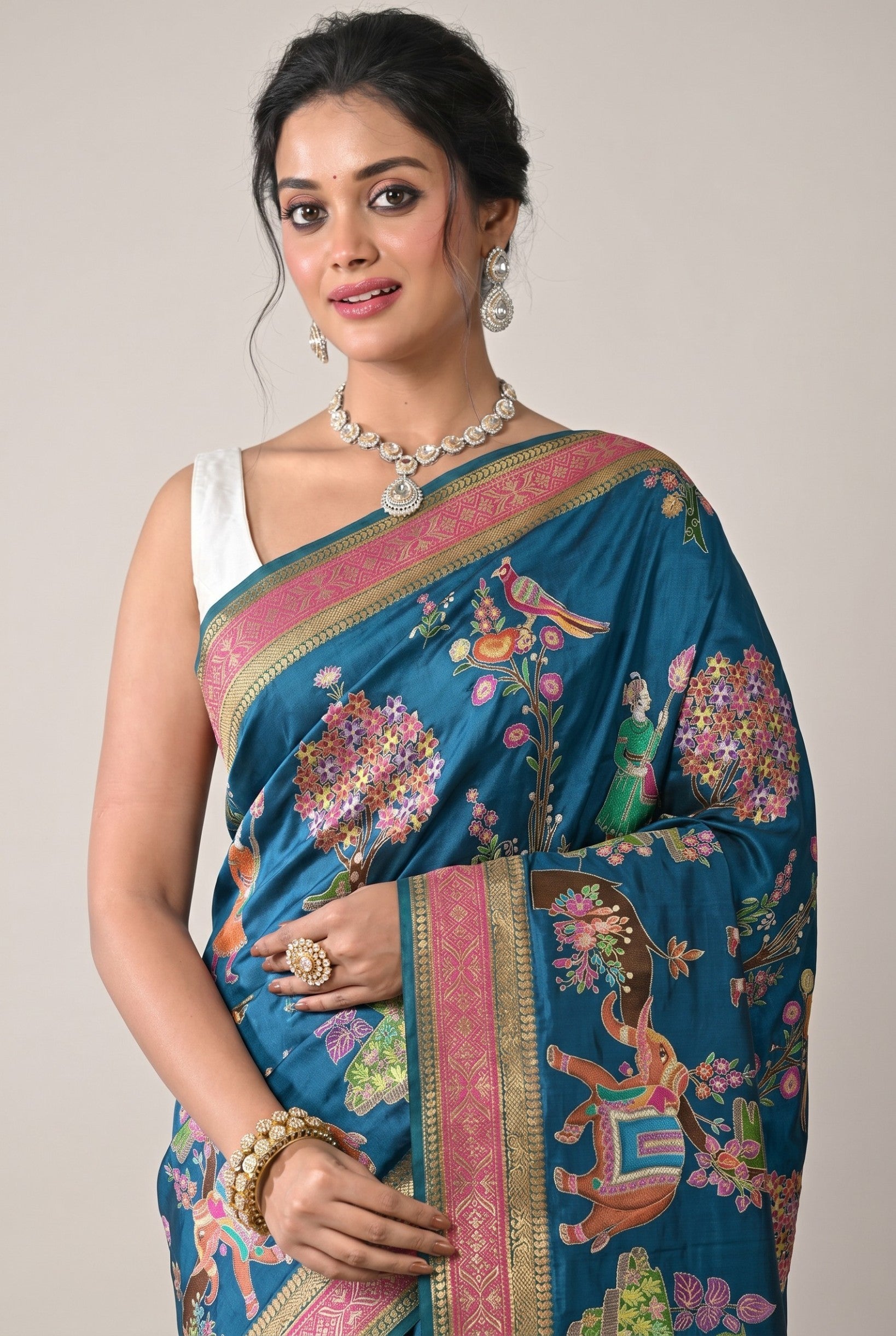 Rangoli teal silk saree with all-over elephant, bird, and floral motifs. Pink and gold border.