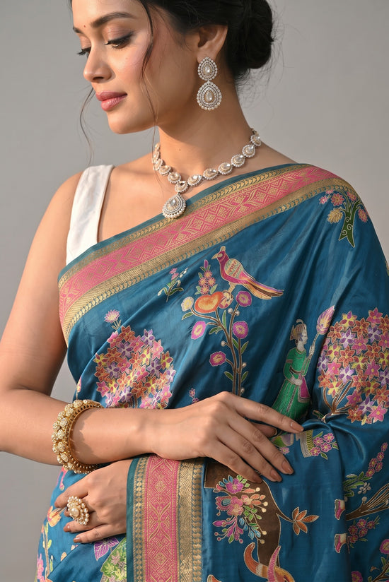 Rangoli teal silk saree with intricate pink and gold border, featuring whimsical elephant, bird, and floral motifs.