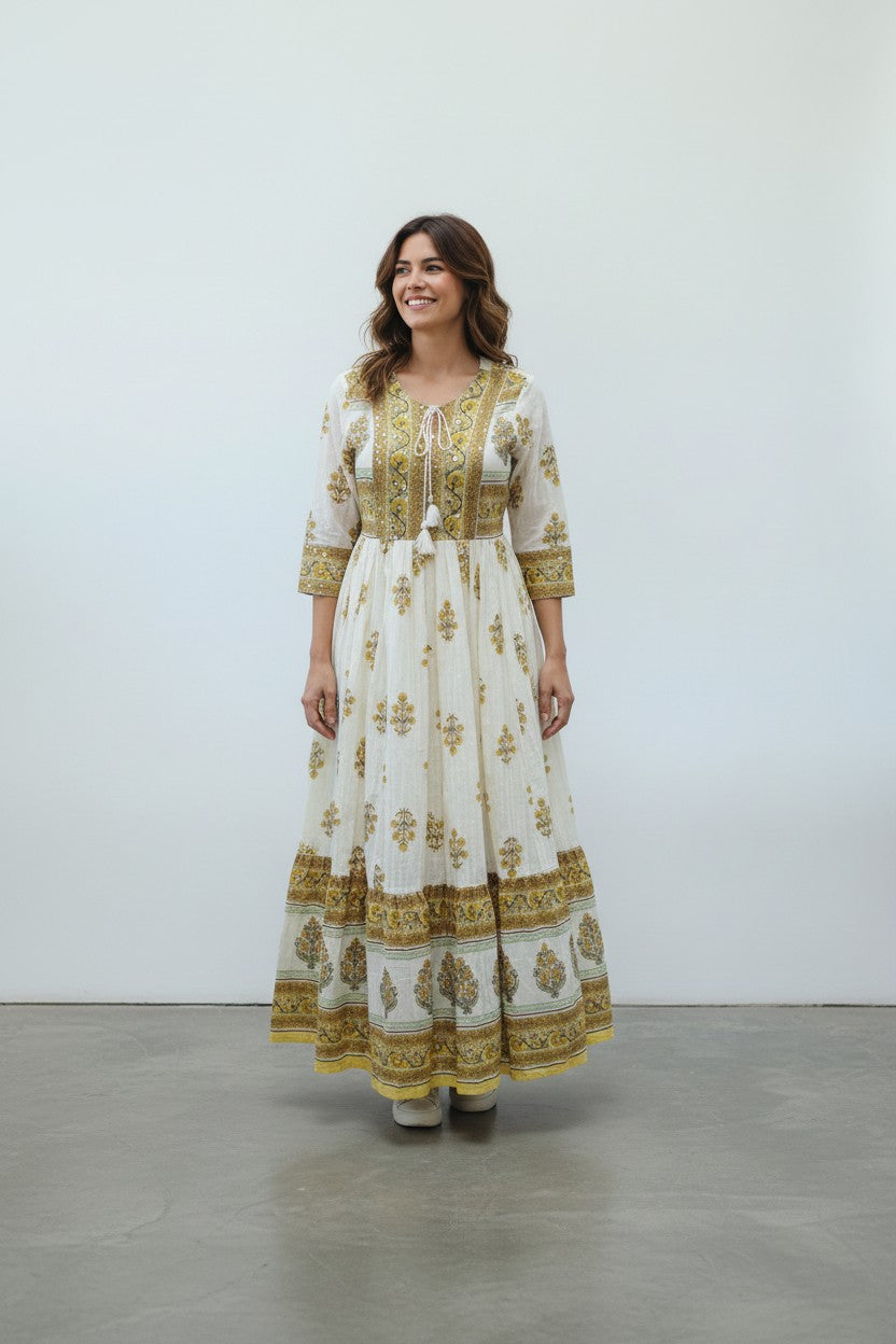Rangoli white cotton maxi dress with yellow and green floral print, V-neck, tassel tie, and tiered skirt.