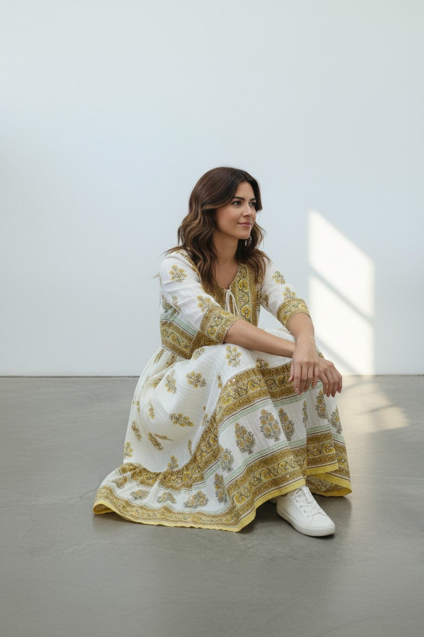 Rangoli white cotton maxi dress with yellow and green floral print, V-neck, tassel tie, and tiered skirt.
