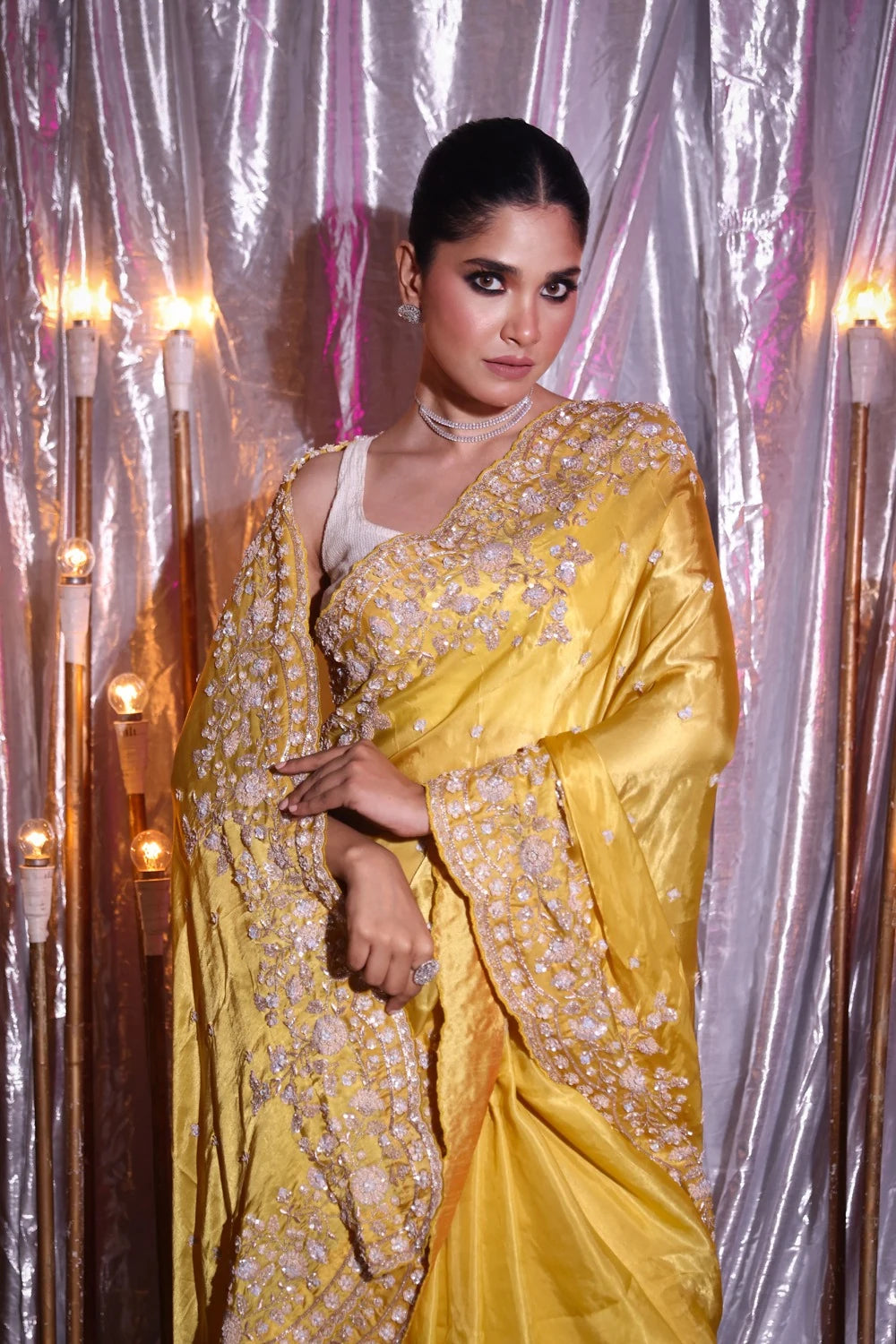 Woman in a yellow saree with silver patterns against a decorative backdrop