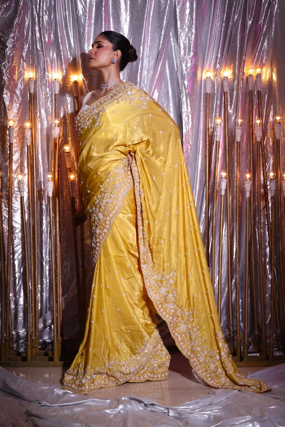 Woman in a yellow saree with gold details against a decorative curtain background
