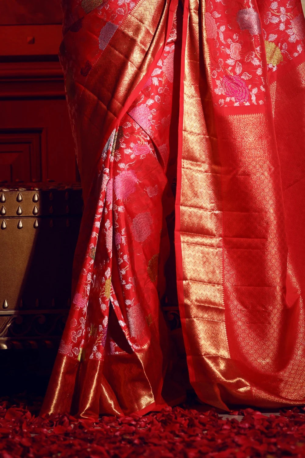 Red saree with gold patterns draped over a wooden surface