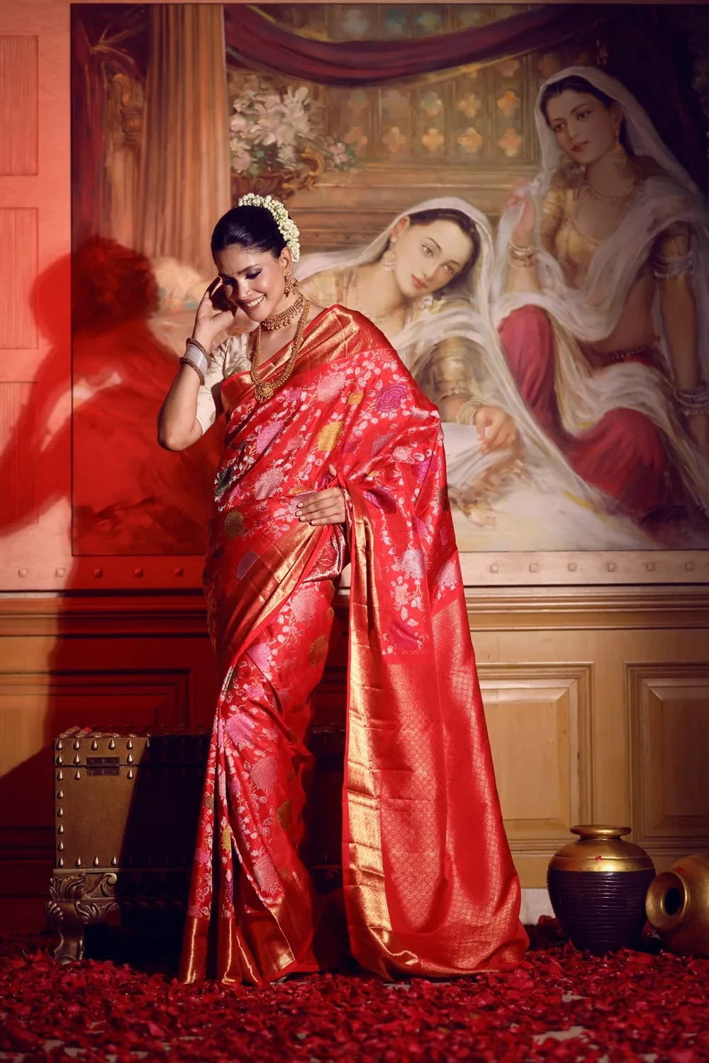Woman in a red saree standing in a room with classical painting in the background